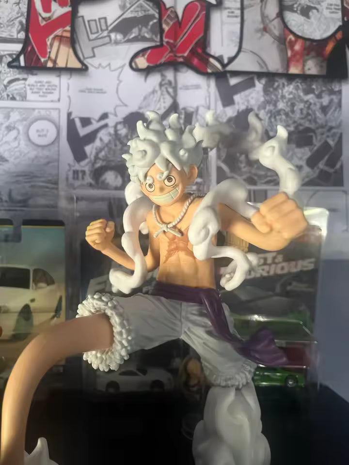 Figura de acción Monkey D. Luffy Gear 5 - Linea Grandista (Banpresto) exhibida frente a fondo de manga, destacando su diseño detallado y expresivo.