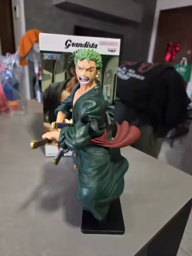 Figura Roronoa Zoro - Colección Grandista (Banpresto Original) en exhibición sobre mesa, con caja de fondo. Ideal para coleccionistas de One Piece.